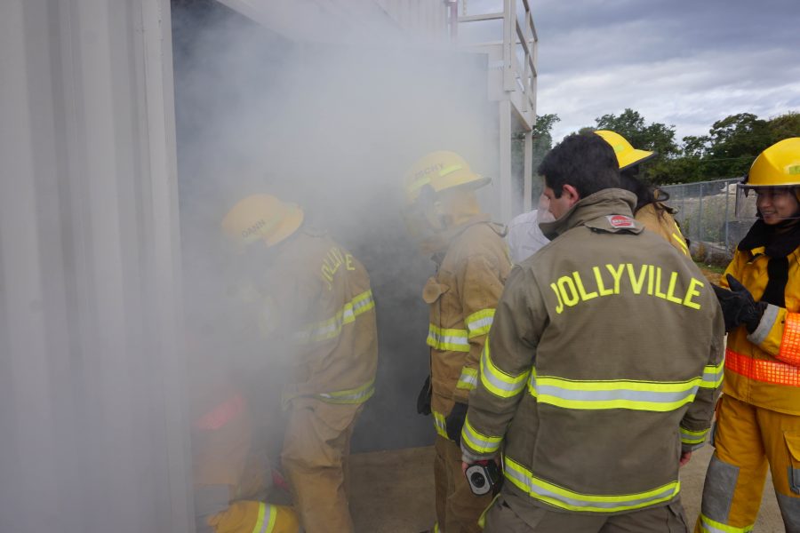 A firefighter observes as a group crouches down to begin their sweep of the smoke filled room.
