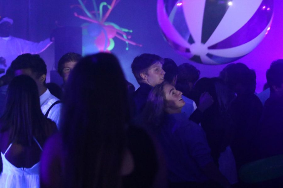 A large beach ball bounces through the black lit crowd. 