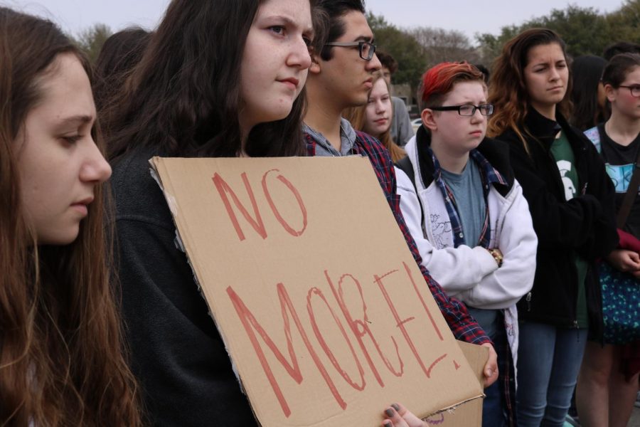 A student listens to the speakers while holding a sign. 