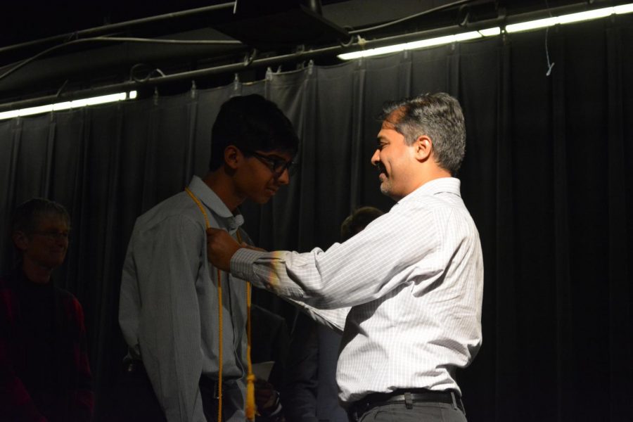 A father smiles proudly as he places a cord around Rushil Udanis 20 neck.
