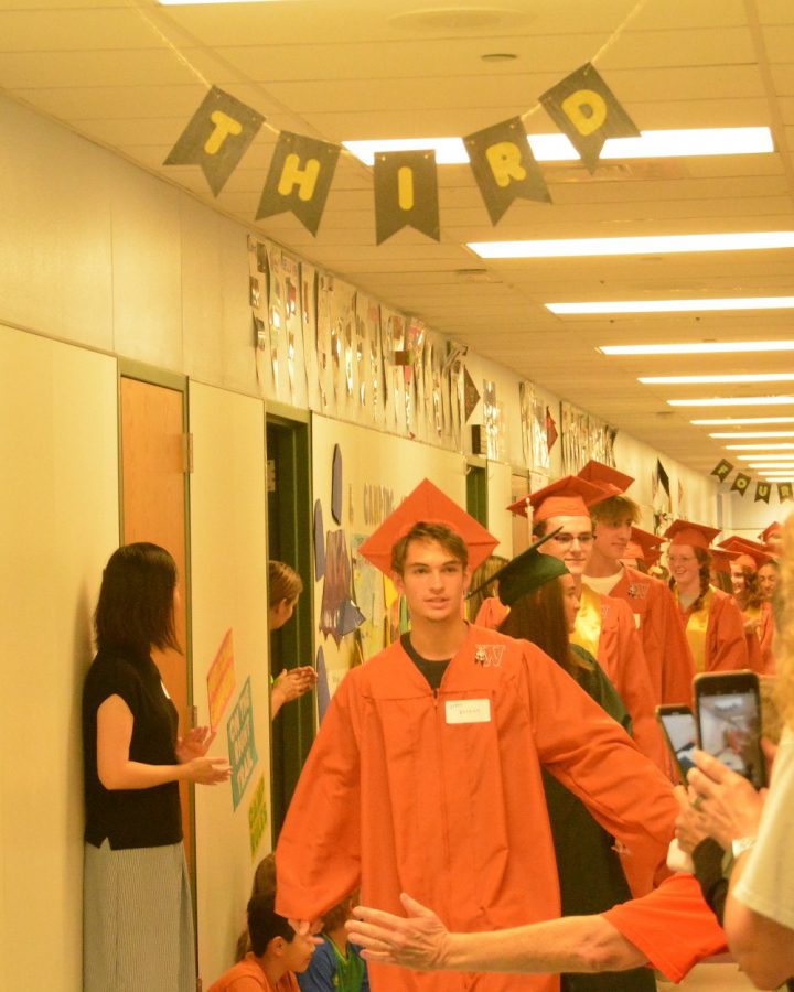 Seniors walk down a hallway as parents, students, and teachers congratulate them.