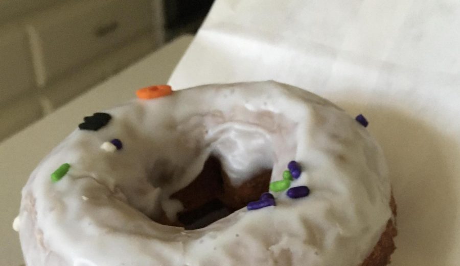 Pumpkin Spice donut from Donut Hub with Halloween themed sprinkles sits on a napkin just ready to be eaten.