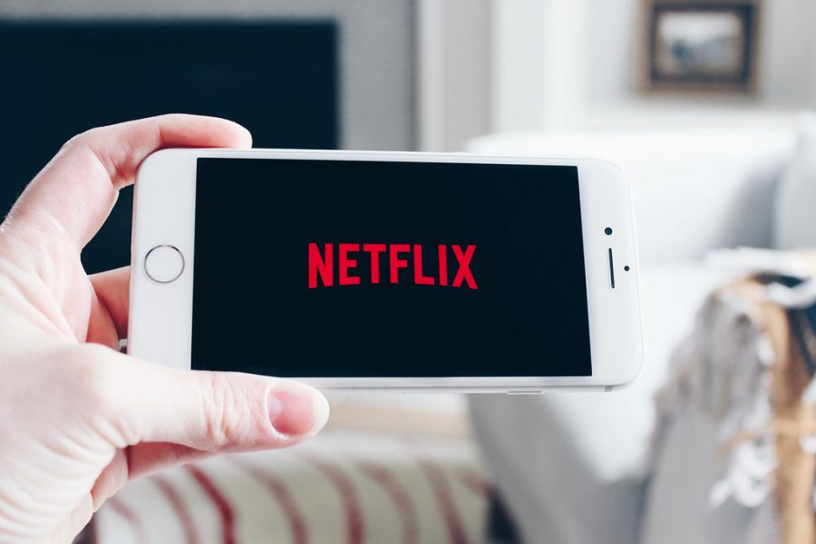 A hand holds a cell phone that displays the Netflix loading screen.