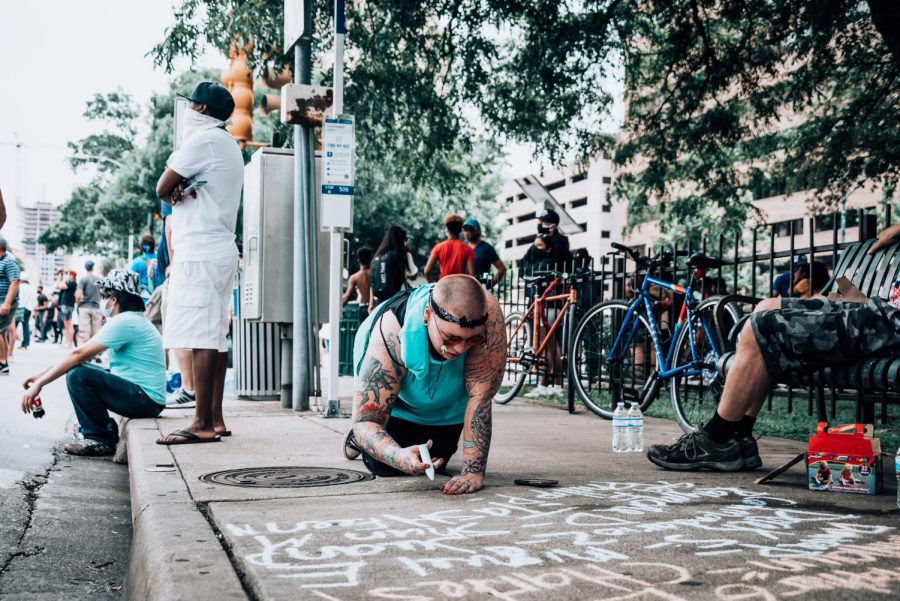 Looking at her phone, a protestor writes a quote with chalk on the streets of downtown Austin. While writing she shared stories of the protests the occurred the previous day with the people around her. 