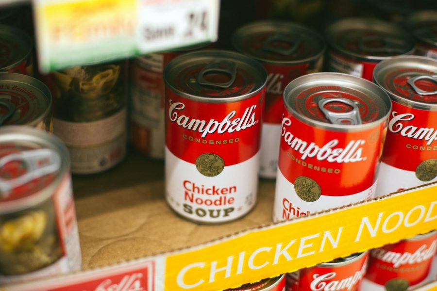 A photo of soup cans on cardboard. Many in the community are struggling to get essential supplies such as food in the current COVID-19 crisis. The local food bank has been working to ease this struggle.