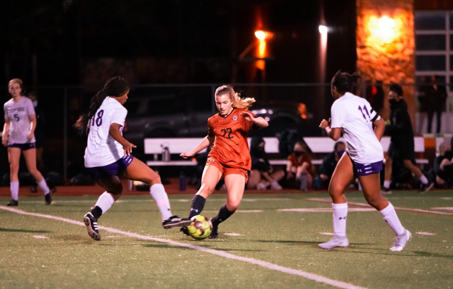 With two opposing players on each side, forward Katelyn Woodruff 21 attempts to dribble the ball around to maintain possession. Woodruff would make a pass to another teammate.