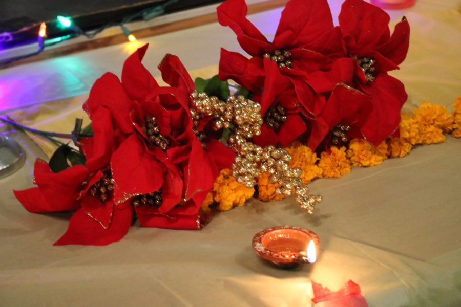 The decorations at the Diwali event were vibrant, bright, and fiery. The flowers on the tables were red and gold, and came with green leaves and gold berries. The diya seen in the bottom of the photo held real fire, which helped brighten and bring life to the event, along with the other decorations.