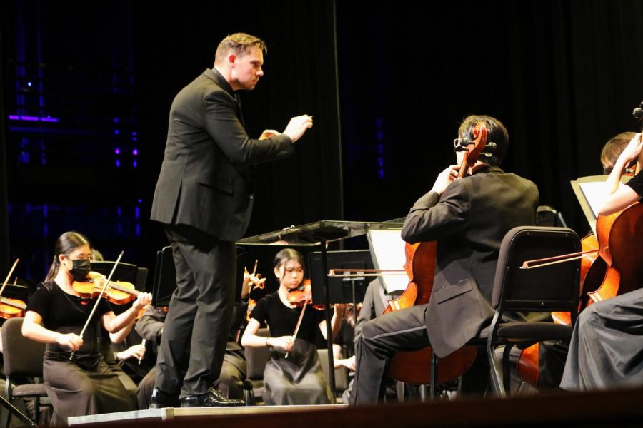 Turning to give a cue, Associate Director Mr. Justin Anderson aids the cello section of the Philharmonic 4th Block Orchestra in making a defined entrance during their performance of Mourão. Written by Brazilian composer César Guerra-Peixe, the piece features a lively central theme alongside isolated figures that highlight different instruments. 