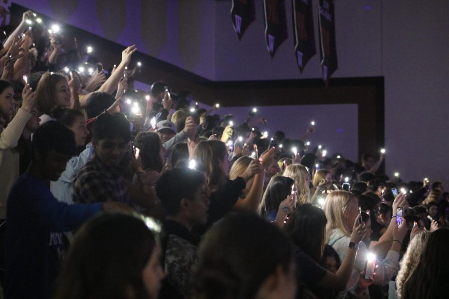 Students shine their phone flashlights in the bleachers. With the accompaniment of glow sticks and flashlights, students committed to the theme of the blacklight pep rally ahead of the final football game of the year. 