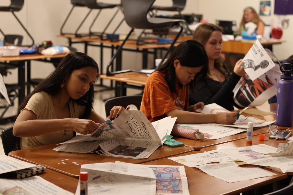 Freshmen Diya Shakkottai and Serena Liu search for words to add to their poems in newspapers. Shakkottai laid out and planned her entire poem before beginning to glue it down.