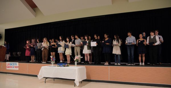 Standing on stage, National French Honors Society (SHF) inductees hold their candles and listen to a speech by president of SHF Nitya Khurana 24. Proudly inducting new members, Khurana highlighted the value of continuing on learning the French language.
