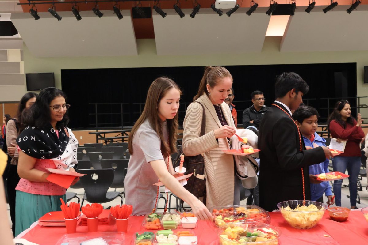 Reaching for a spoon, Deborah Gutierrez 25 serves herself fruit following the induction ceremony. Food such as chips and salsa, taquitos, and cake were served to new inductees and their families. 