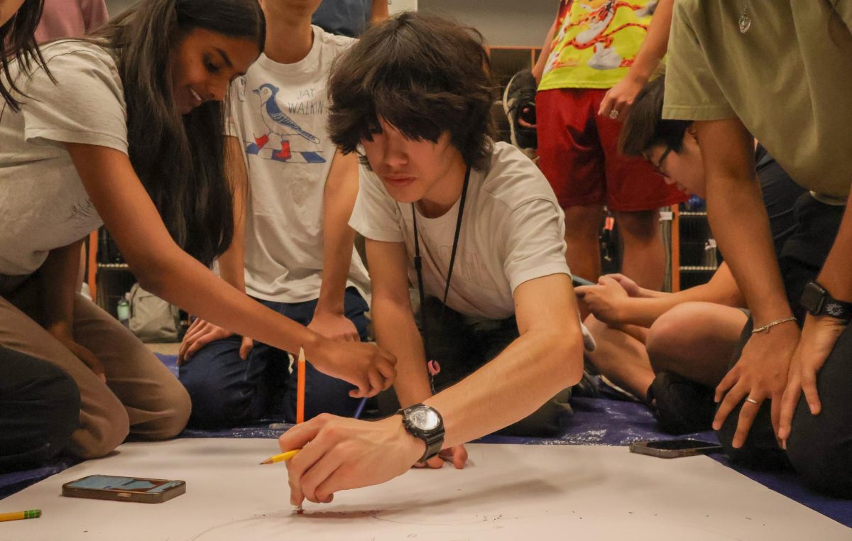 Crowding around a poster board, Junior cellists Samhita Guntakala and Sam Yarbrough refine their sketch of a cello. Over the span of an hour and a half, the cellists worked together to bring their section poster to life. "Every year, we always draw a cello in some sort of different situation, and this year [it's] a cello wearing concert black on a stage," Yarbrough said. 