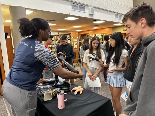 A crowd of intrigued students gathers at the Hanger Clinic booth, with one eager student Youjia Yu '28 examining a prosthetic limb up close.