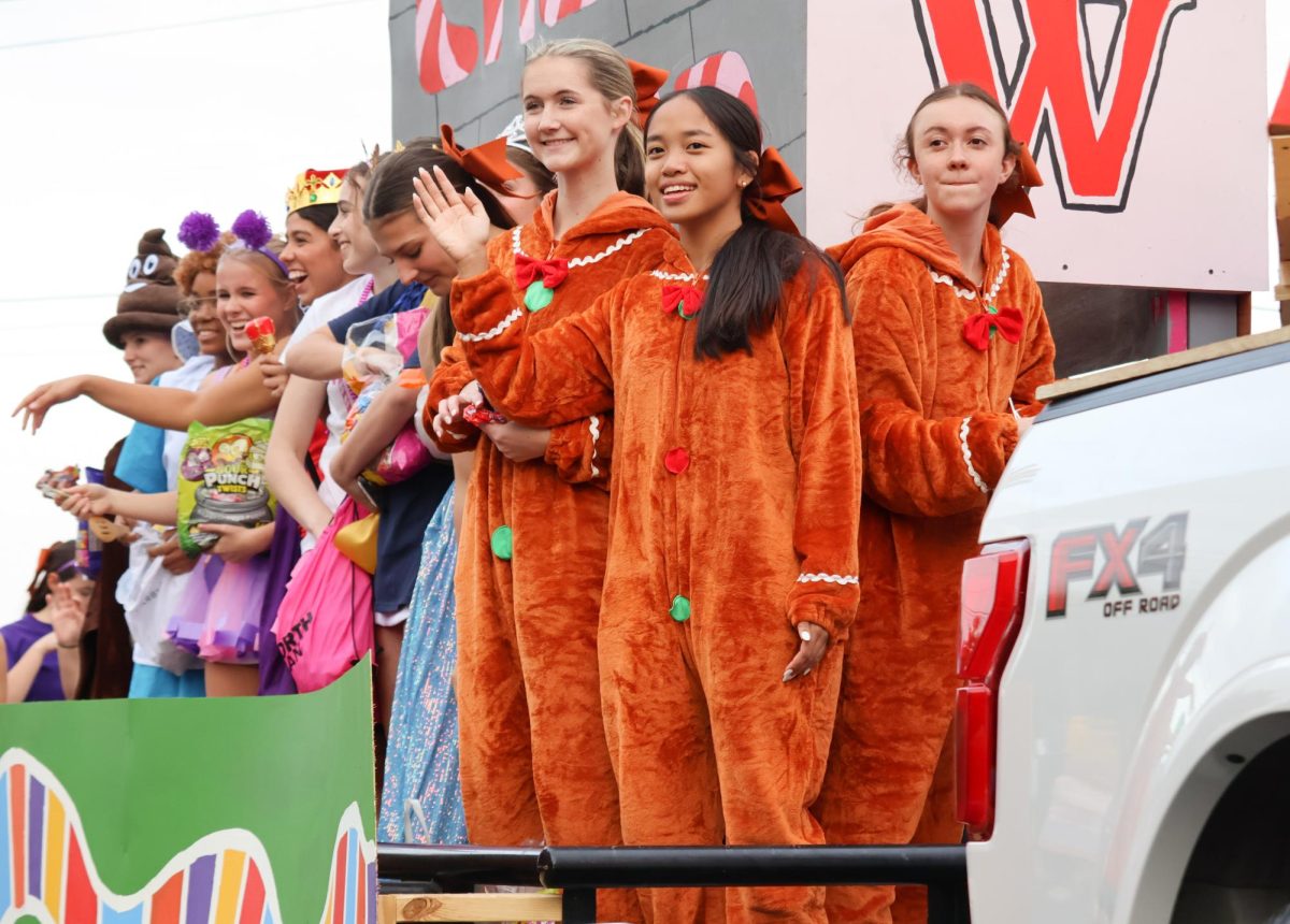 Waving to the crowd, Warrior Cheer throws candies and chocolates to the children lining the streets. Cheer adopted the theme of Candy Land for their float, eventually winning first prize for their float design and execution. 