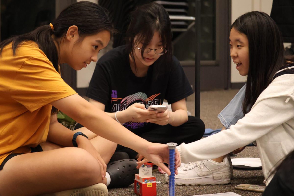 Sitting in a circle, Adriana Cheng '26, Jenny Yun '25, and Hannah Lee '26 engage in a game of 5 Second Rule. With a marble timer and a stack of cards, they were able to enjoy the afternoon with excitement.