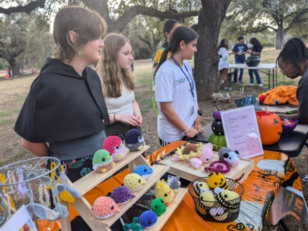 Standing behind their decorated booth at the Spooktacular, Fiber Arts Club members entertain a customer during one of their sales. The club sold a variety of personally-crafted plushies and key chains during the event. 