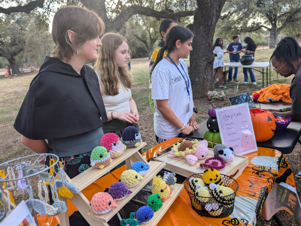 Standing behind their decorated booth at the Spooktacular, Fiber Arts Club members entertain a customer during one of their sales. The club sold a variety of personally-crafted plushies and key chains during the event. 