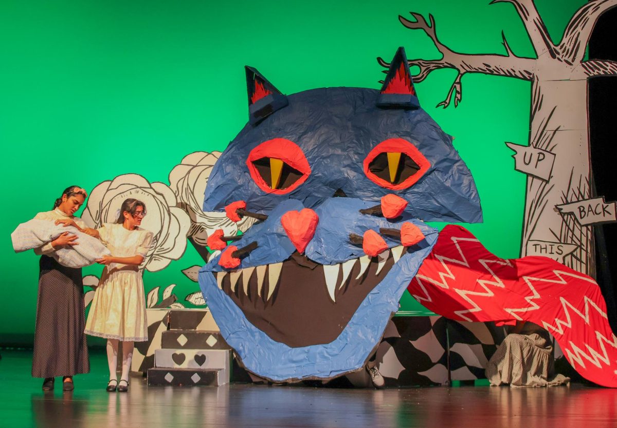 Standing beside the Cheshire Cat, Alice (portrayed by Prishaa Vishwakarma '27) asks for advice on how to navigate Wonderland. The Cheshire Cat was represented by a three-part puppet, designed by technician Dominik Brown '26. "I wanted it to be scary, because in most media he has that creepy smile, and I wanted that but kind of like an angler fish," Brown said. 