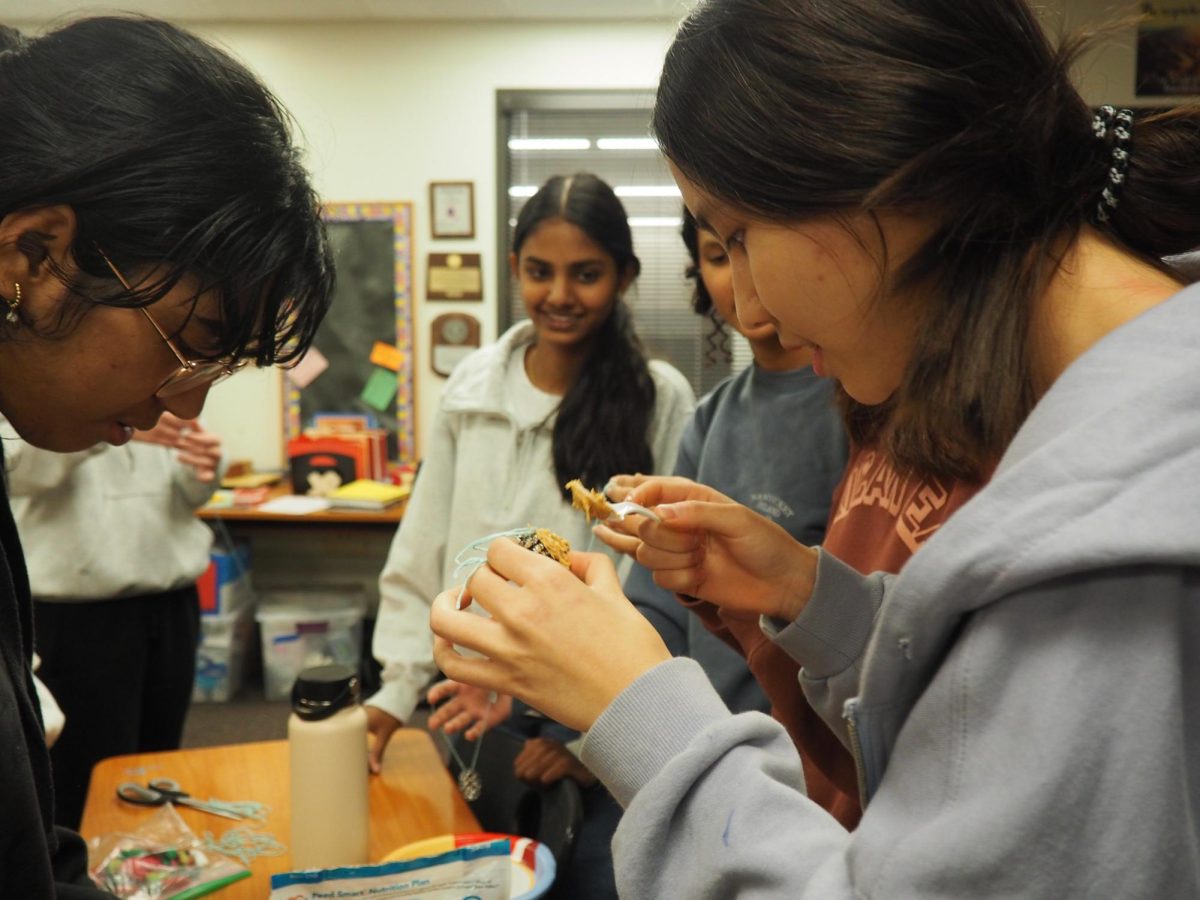 Chatting with friends, Freshman Class President Apple Ma adds peanut butter to her birdseed feeder. The birdseed feeders were given out to volunteers to take home and give to family and neighbors. "I think it's important because it kind of is a good way for you to represent how you want to change the world," Executive Vice President Josie Sun '26 said. "It's not something that I think people are really rewarded for a lot, but I still think choosing to serve others is something that really encapsulates what Student Council is."