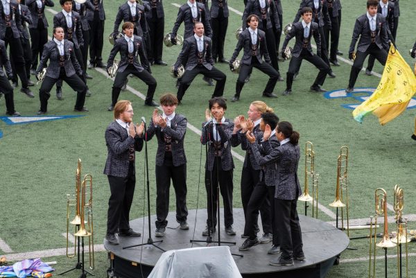 Standing on a stage, the trombone ensemble claps to a beat. The trombone ensemble provides a groove to part three of the band's show Timeless.