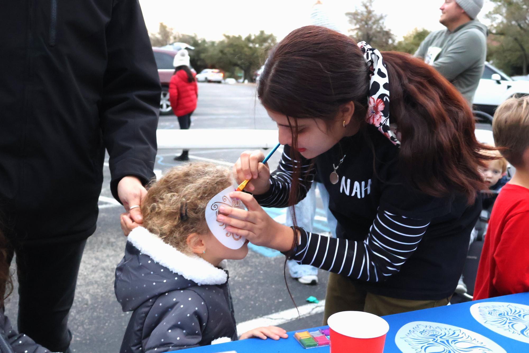 Heavily concentrated, NAHS member Chloe Nanda '27 places a butterfly stencil on the child's face and begins to paint in the lines. With many designs and colors available, NAHS's face painting booth grew in popularity as the evening went on and countless children lined up.