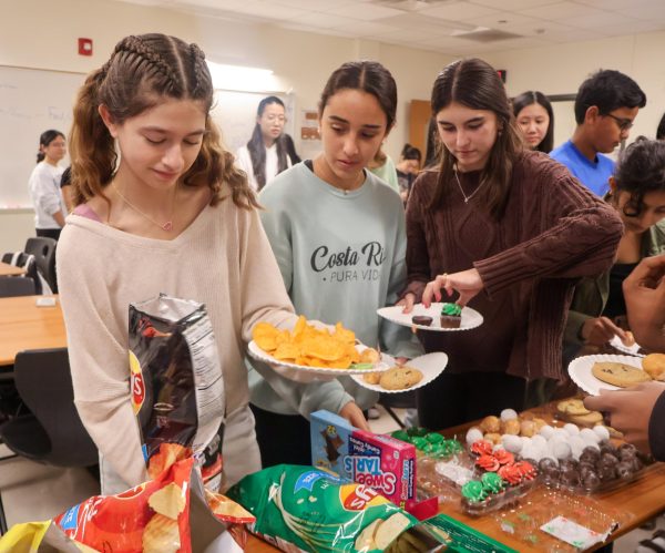 Excited, Millie Sardan Toro '28 fills her plate with chips at the beginning of the winter social as freshmen Lina Saad and Ana Schiemer watch. Going to the social as a friend group, the trio later made their gingerbread house together.