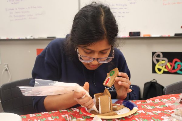 Focused on her creation, Sanjana Iyer '25 frosts her gingerbread house to hold her door. The stability of the house was a key criteria in the judging as were other components like creativeness and visual appeal.