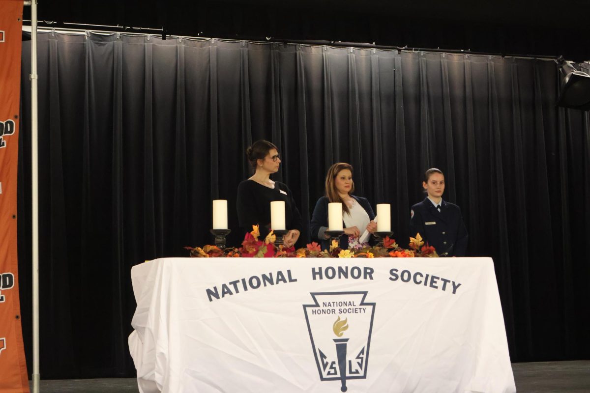 Standing on the stage, Associate Principal Sarah Lowery, NHS Sponsor Christin Key, and Aleks Tremmel '25 prepare to hand out certificates. Officers worked to set up the stage for the ceremony an hour before it began.