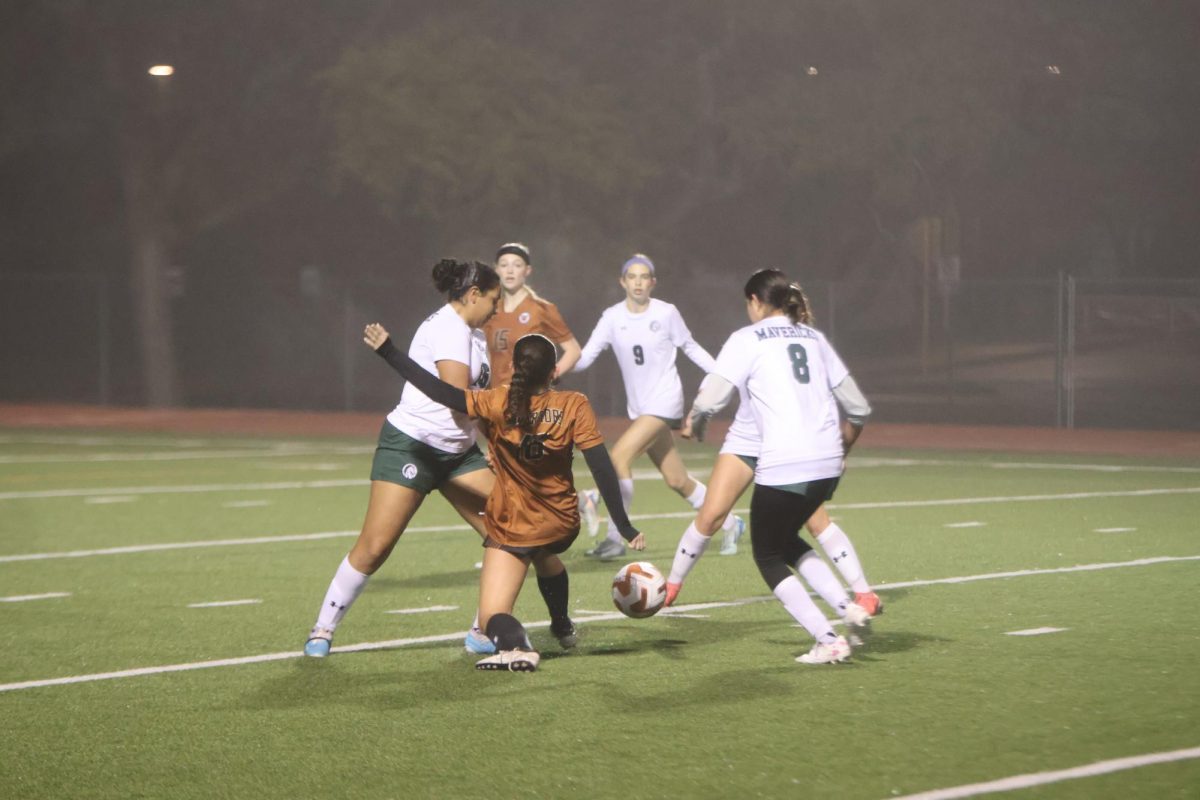 Sliding under her defender, Jaelynn Solis '27 attempts to kick the ball to space while fighting against the wet slippery ground. The Warriors played against Mcneil while facing the rain and freezing temperatures but continued to keep the ball moving in order to stay warm and active.