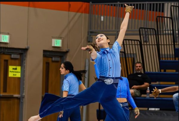 Leaping into a pose, Alycia Chee '26 performs her solo at the beginning of the Varsity Color Guard's 2025 production "And I think to myself..."