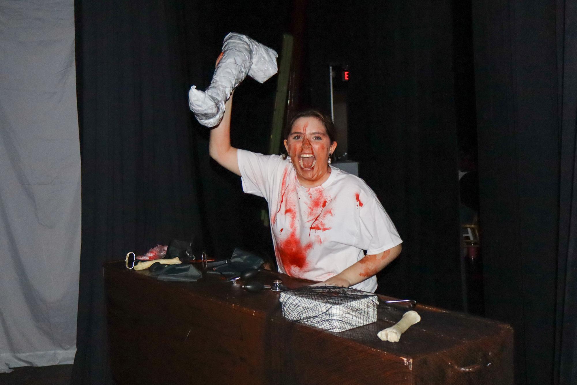 Raising a paper mache limb above her head, Kymber Tribou '28 performs a jump scare. As both a member of the planning committee and a scare actor, Tribou was very involved with the haunted house process. 