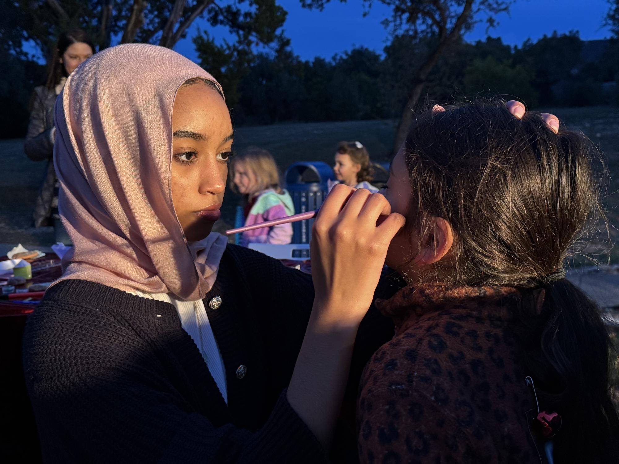 Carefully holding her muse's head, Dalia Ahmed '28 paints a snowflake design on the girl's face. While other kids waited in line, they browsed the paper with different designs that the National Art Honor Society (NAHS) provided. "I feel like coming to do face painting helped me better interact with younger kids by simply talking to them and getting to know them," Ahmed said.