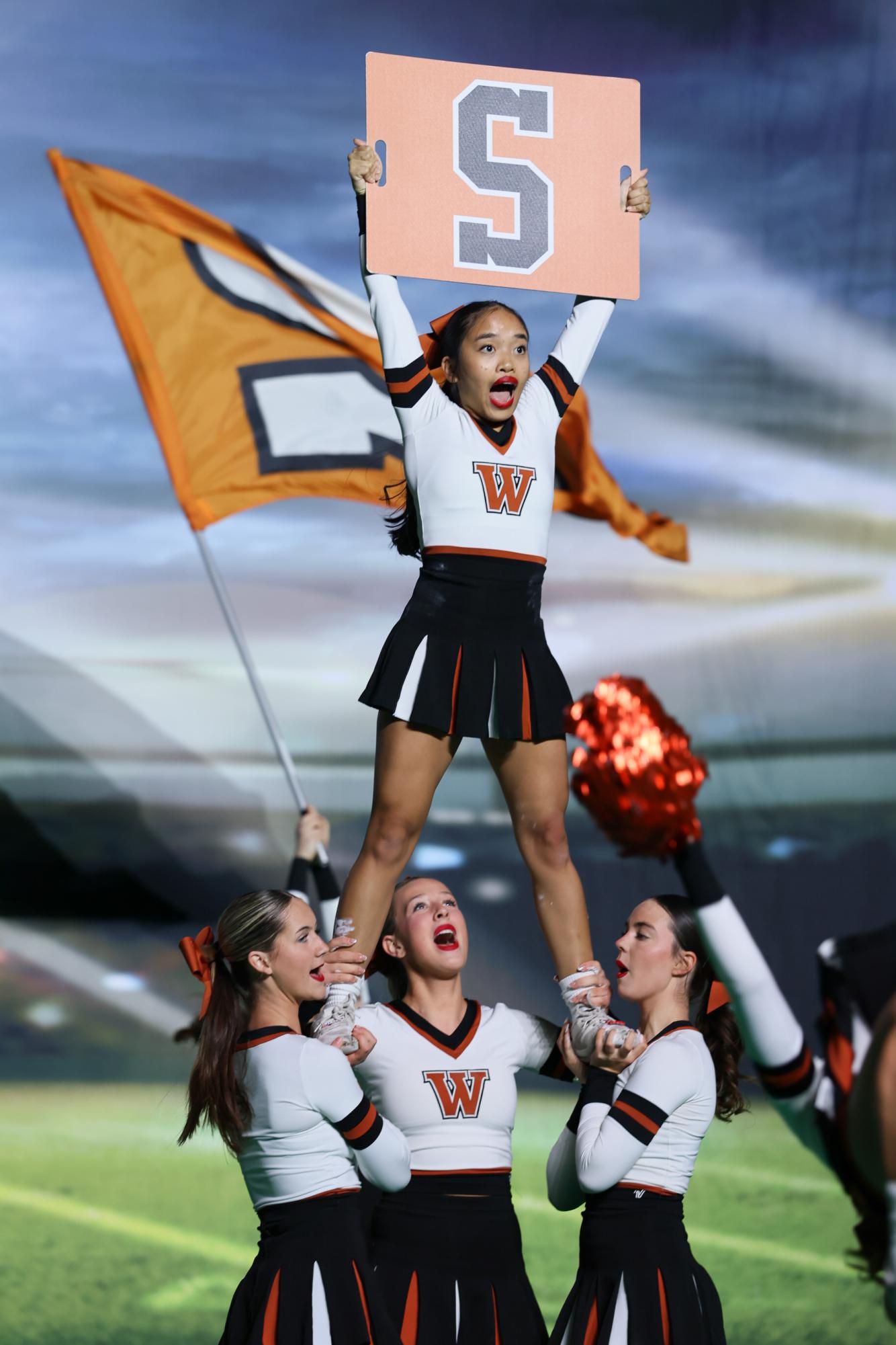 Raising up a black an orange sign with the letter 'S,' Melody Nielsen shouts as she is being held by Katelyn Wiley '27, Amelia Williams '27, and Emery Stevens '27. Their surrounding teammates supported each other by uplifting each other's spirits before and after their performance. “My motto is fake it ‘til you make it,” Nielsen said. “Even though I’m really nervous beforehand and during, I still try to make sure that I keep myself in the moment and that I’m able to do my part throughout the routine so I can be the best cheerleader I can be.”