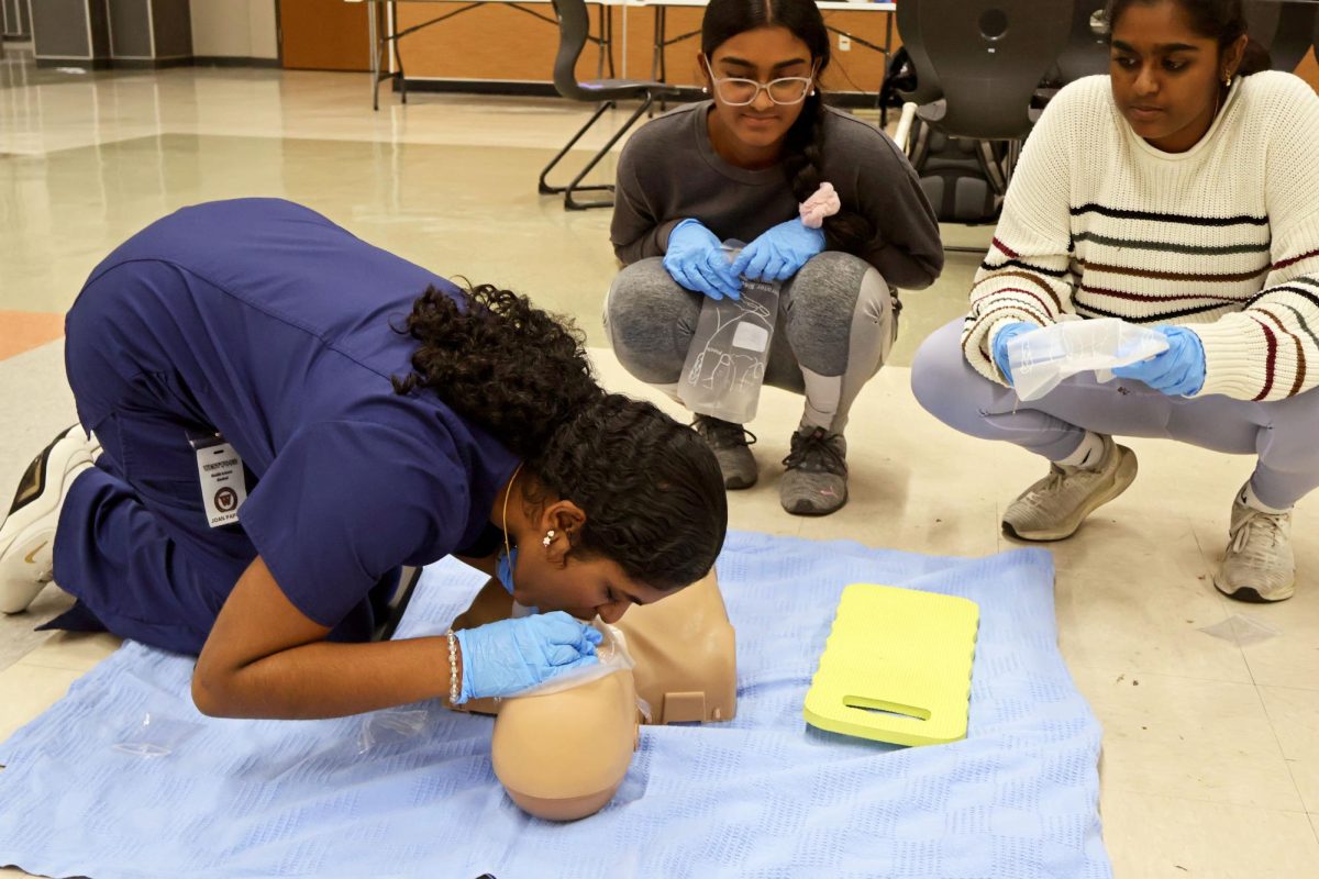 Blowing into a dummy's mouth, Joan Amalraj ’27 practices giving breaths to a CPR manikin as Red Cross Club members wait their turn. The hands-on activity helps students learn proper lifesaving techniques and build confidence in emergency situations, preparing students to respond quickly and safely when someone needs CPR.