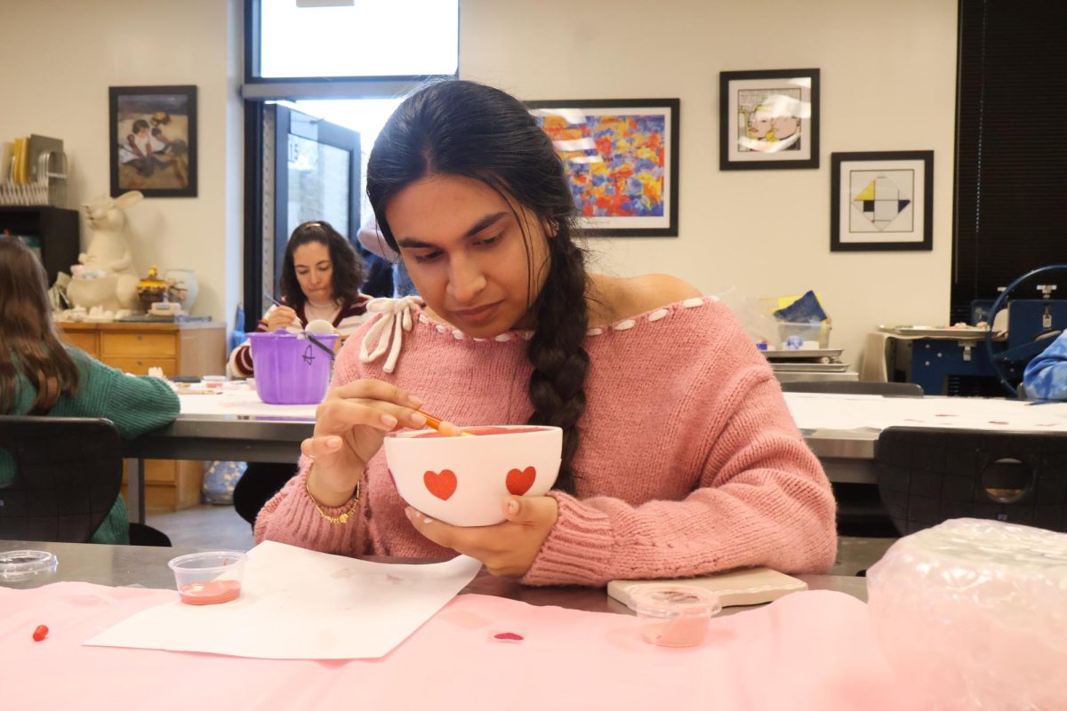 Focused, Ceramics Club Treasurer Maggie Arora '27 paints the inside of her bowl with pink glaze. Before the fundraising event, officers set up different stations for each table, including varying supplies such as stick-on hearts and different glaze colors.