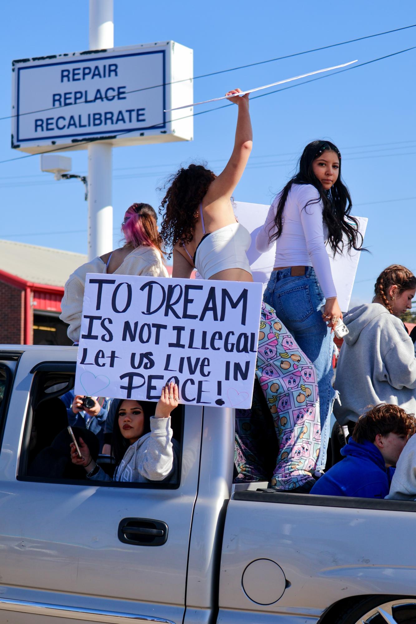 Hands raised, students stand in a truck holding a sign reading "To dream is not illegal, let us live in peace." The sign was of many referring to former President Barack Obama's Deferred Action for Childhood Arrivals (DACA) policy, a policy intended to protect undocumented young adults, deemed 'dreamers.' 