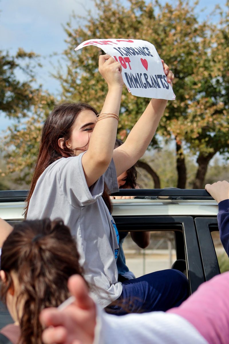 Sitting in a car, Marley Huston '26 holds a sign reading "Fight ignorance, not immigrants." Huston's poster refers to the belief that hatred for immigrants stems from ignorance of the country's indigenous history and the world's past genocides that parallel current immigrant persecution.