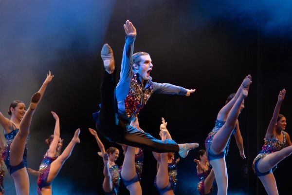 Performing a leap mid-air, Elliott Richards '26 leads a group dance sequence on stage. Richards brought 15 years of competitive dance experience to the stage, having practiced his technical skills since he was a child.