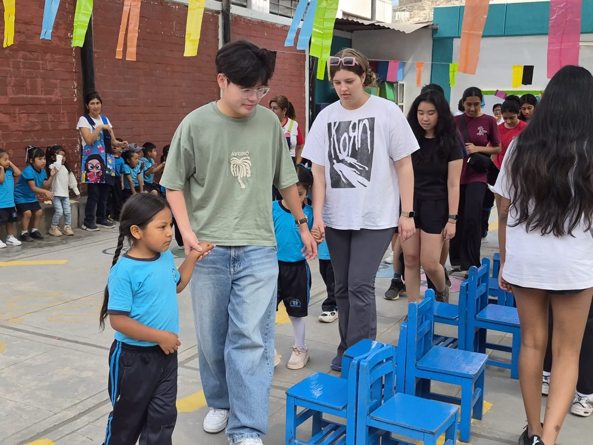 Walking around tiny blue chairs, Westwood MEDLIFE Club Vice President Taehyun Kim '27 holds a kindergartener's hand as they join in a game of musical chairs. Hanging out with the younger kids in the Huáycan community was important bonding that fostered a better understanding of their way of life. 